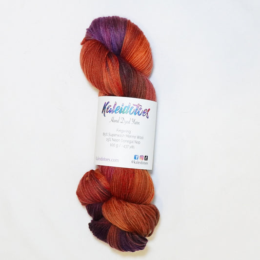 Hand-dyed fingering weight yarn in brick red, burnt orange, deep violet, and magenta with rich swirling color transitions.