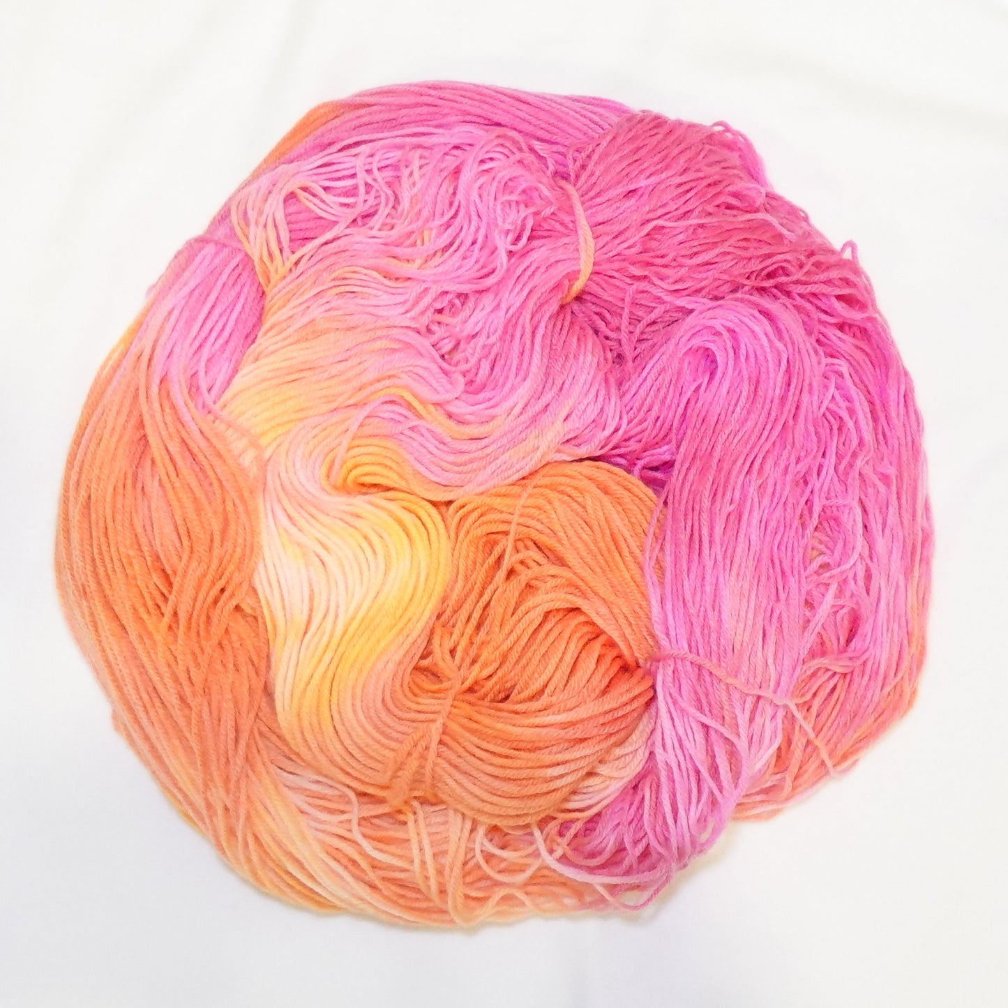 Hand-dyed yarn in soft peach, coral, warm pink, and hints of yellow — blended smoothly like melted taffy candy.