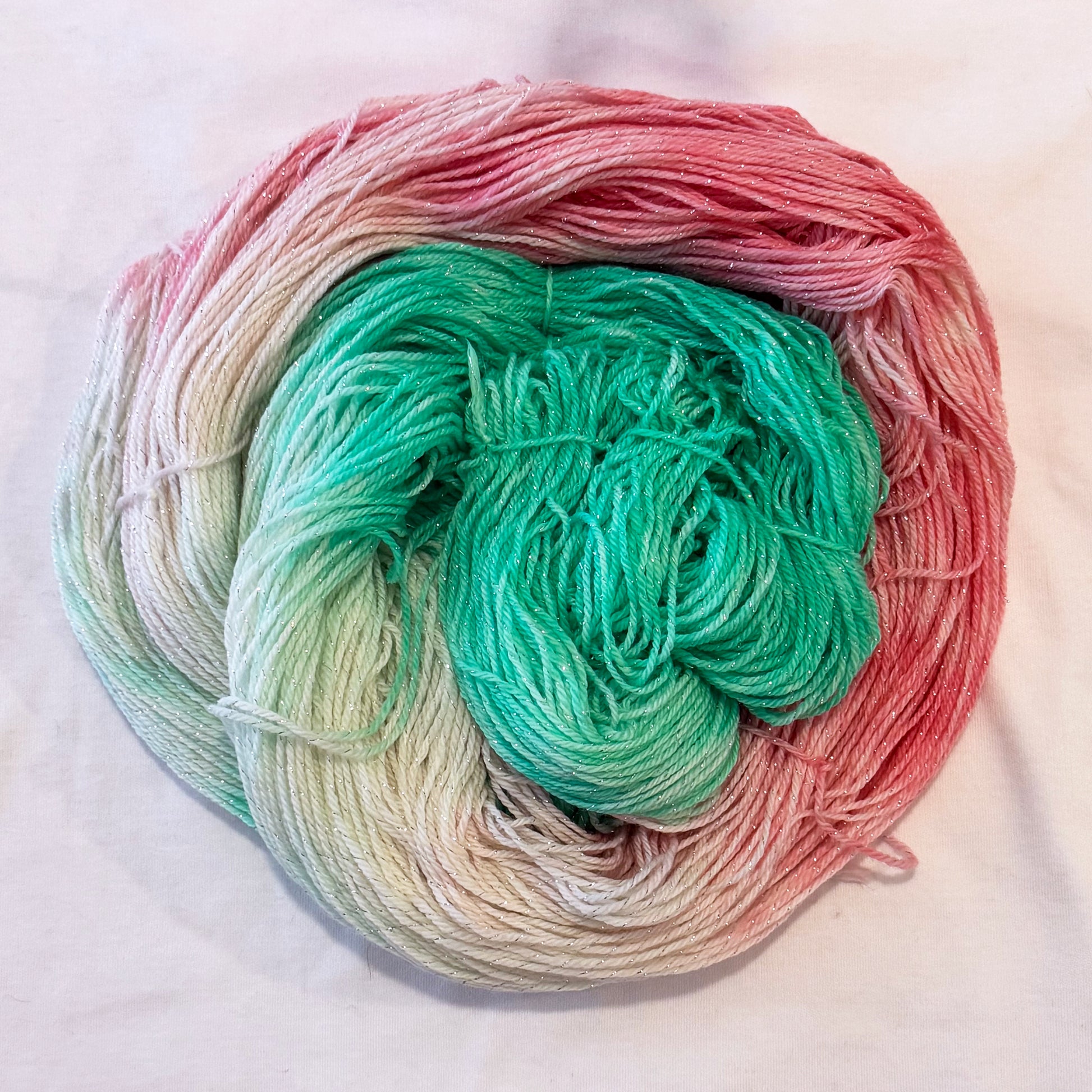 Hand-dyed yarn in mint green, soft pinks, and ivory tones with subtle silver metallic throughout.