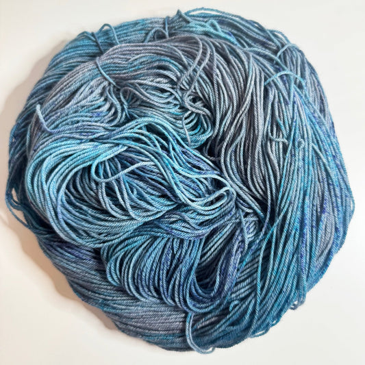 Hand-dyed sock yarn in blue-grey and ocean blue with navy speckles, Phantom Tide colorway