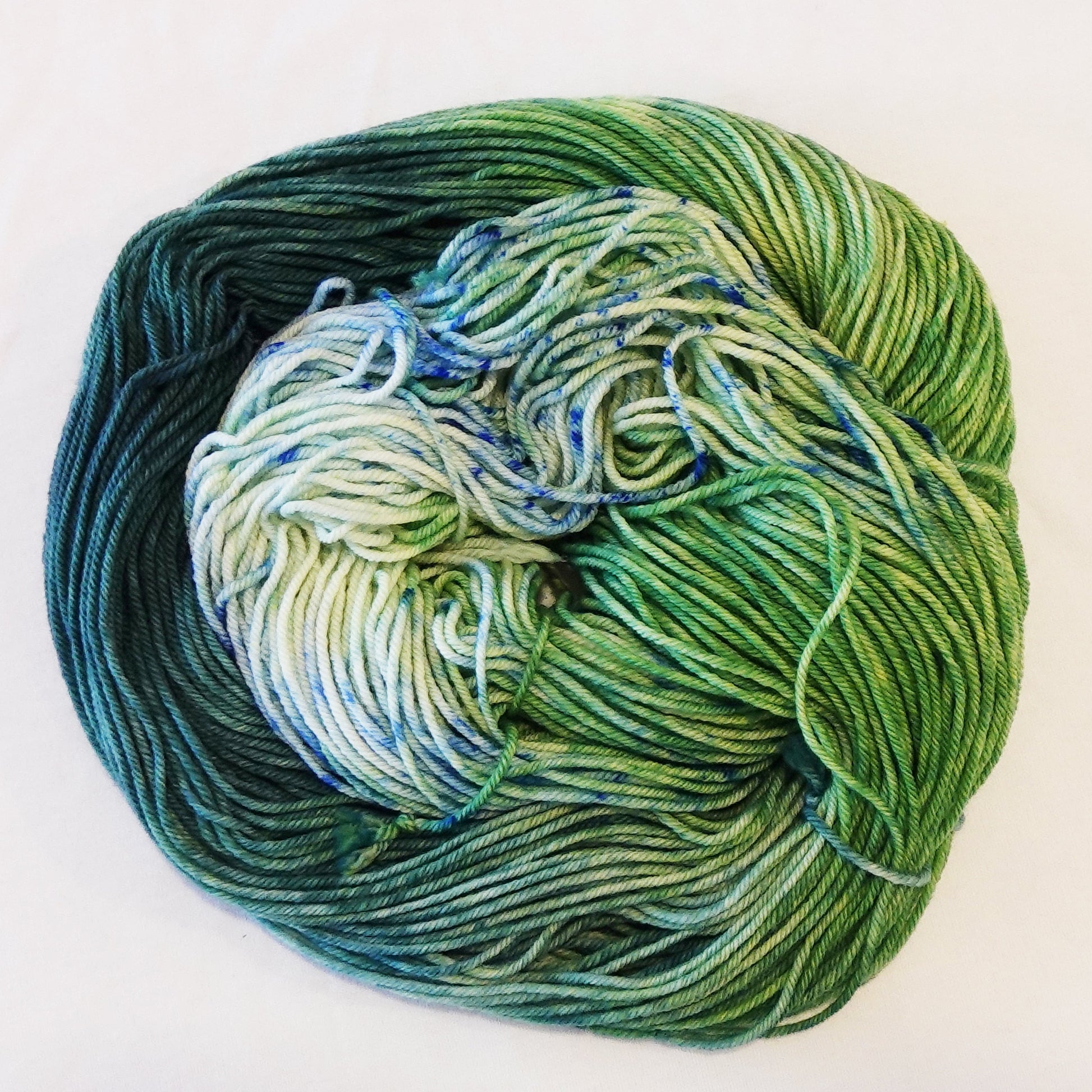Hand-dyed yarn skein in layered teal and green tones with subtle teal and green speckles