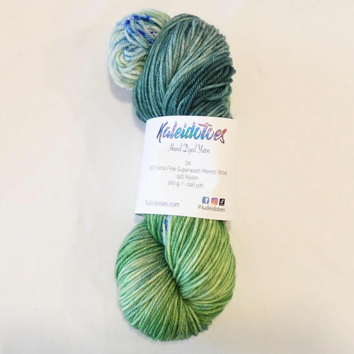 Hand-dyed yarn skein in layered teal and green tones with subtle teal and green speckles