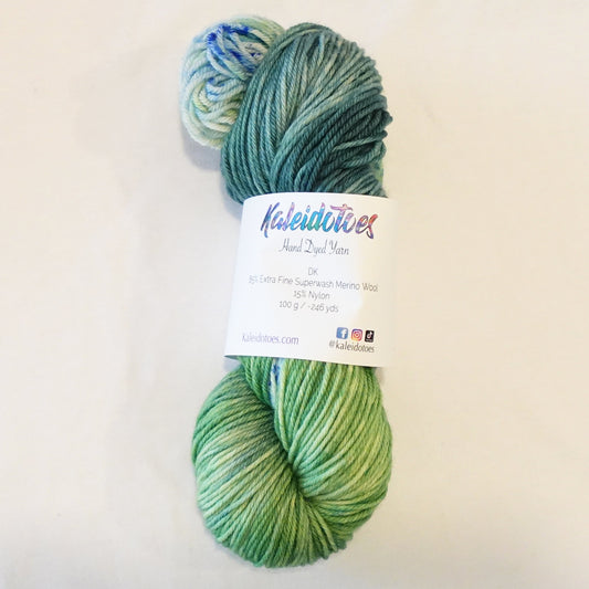 Hand-dyed yarn skein in layered teal and green tones with subtle teal and green speckles