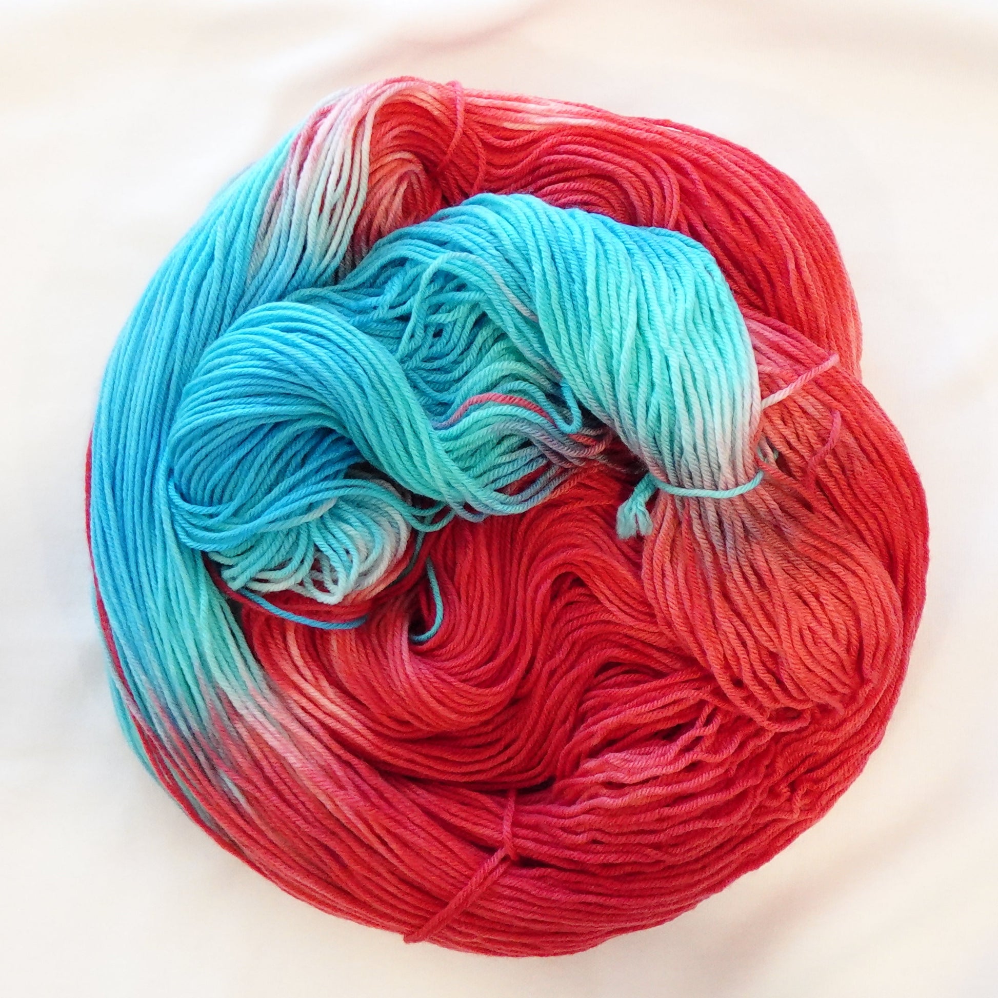 Hand-dyed yarn in bright red, aqua blue, and soft white tones — bold and refreshing like a classic rocket pop popsicle.