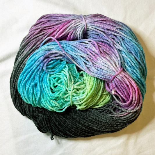Hand-dyed skein of worsted weight yarn in deep charcoal, lavender, soft pink, turquoise, and seafoam green — luminous and layered like stained glass.