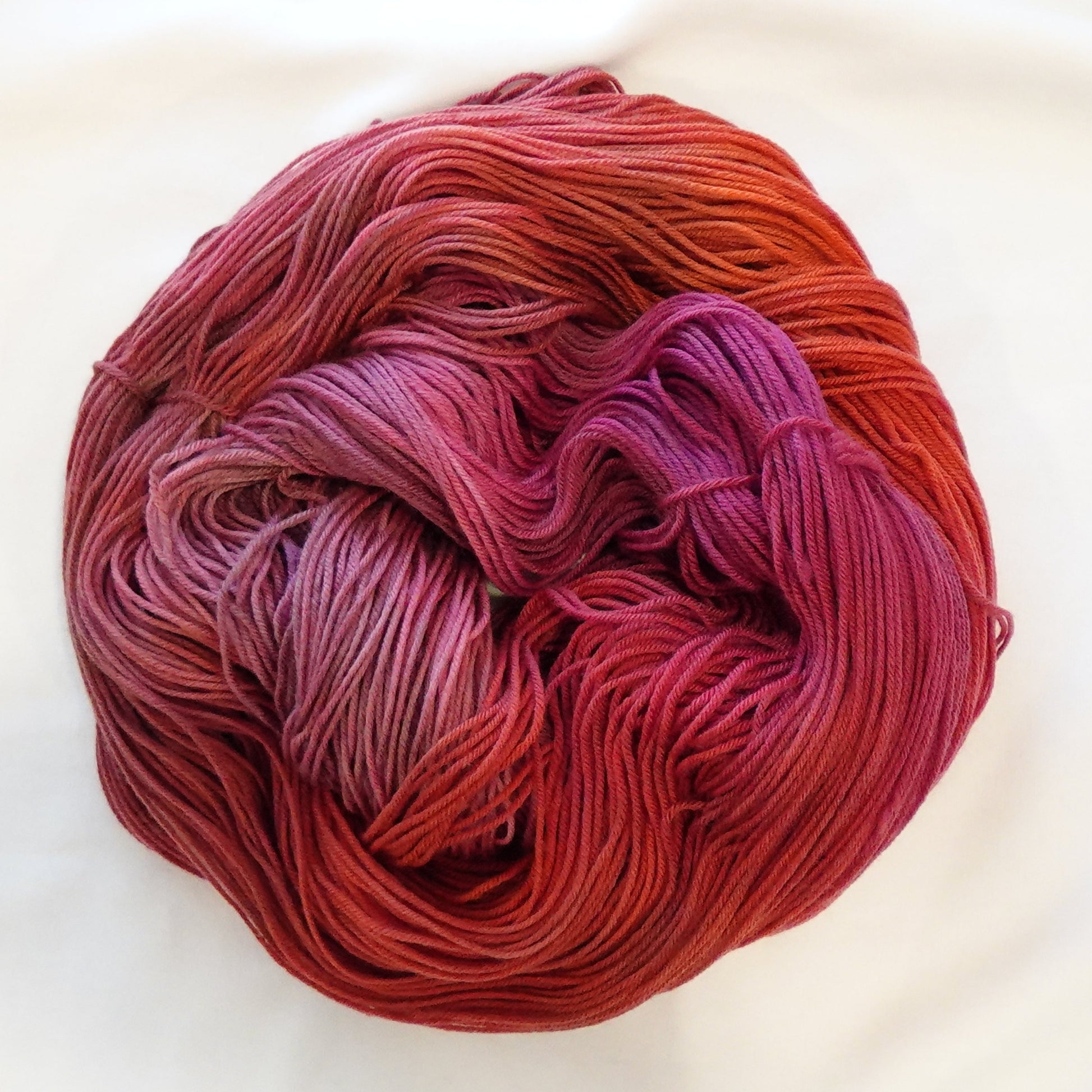 Hand-dyed yarn in deep burnt orange, crimson, raspberry, and magenta tones — richly layered and smoldering with warm depth.