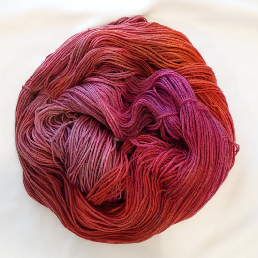 Hand-dyed yarn in deep burnt orange, crimson, raspberry, and magenta tones — richly layered and smoldering with warm depth.