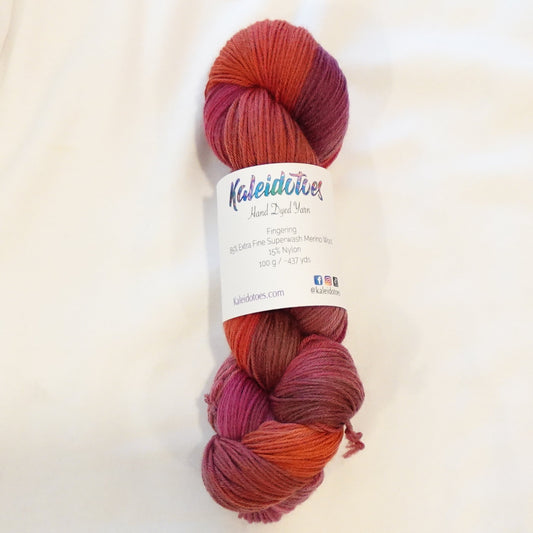 Hand-dyed yarn in deep burnt orange, crimson, raspberry, and magenta tones — richly layered and smoldering with warm depth.