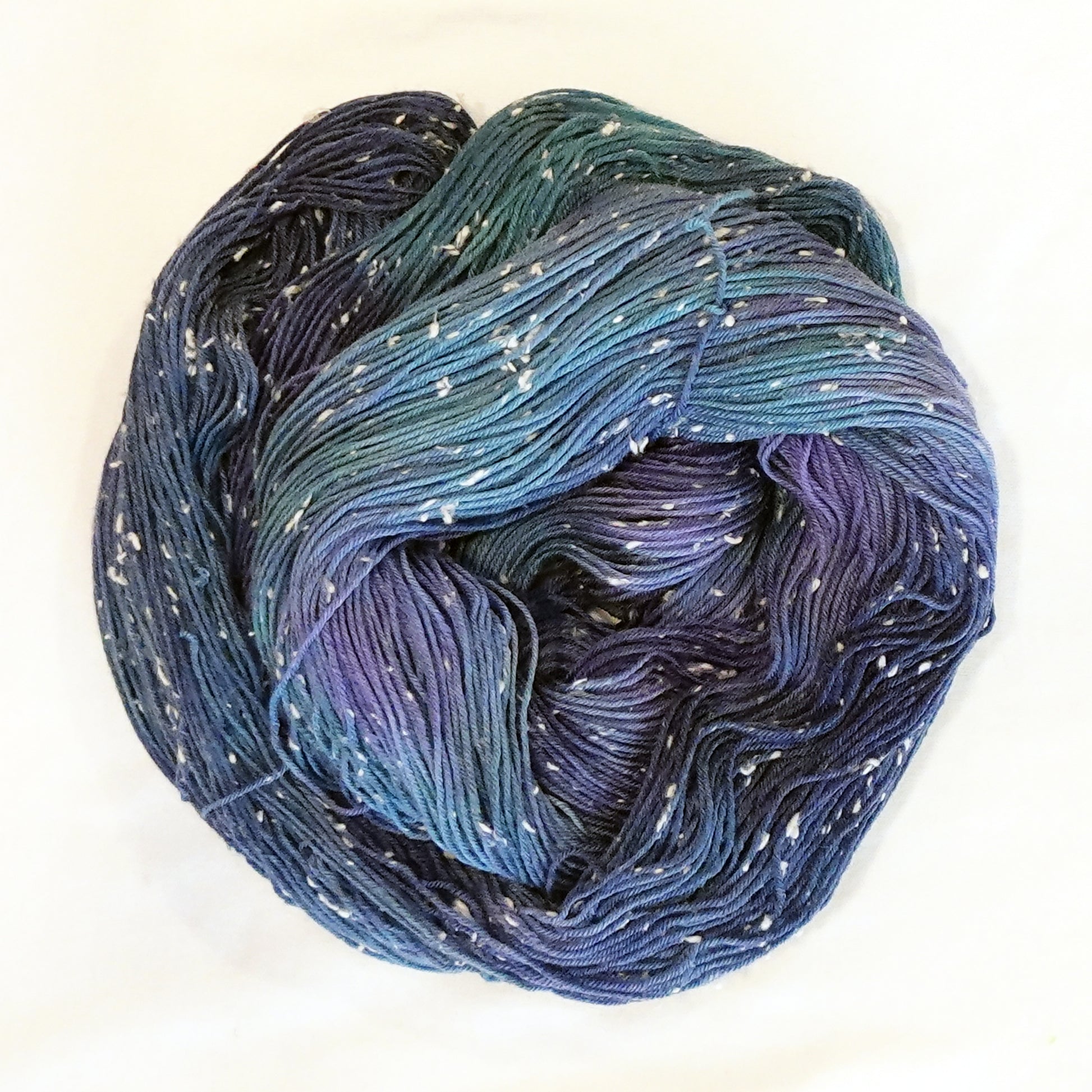 Hand-dyed yarn in shades of deep blue, indigo, and violet with soft white flecks scattered throughout — moody, layered, and reminiscent of a star-filled night sky.