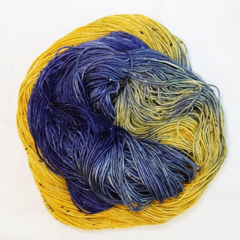 Hand-dyed tweed fingering weight yarn in golden yellow, deep blue-violet, navy and smoky blue-grey with black tweed flecks.