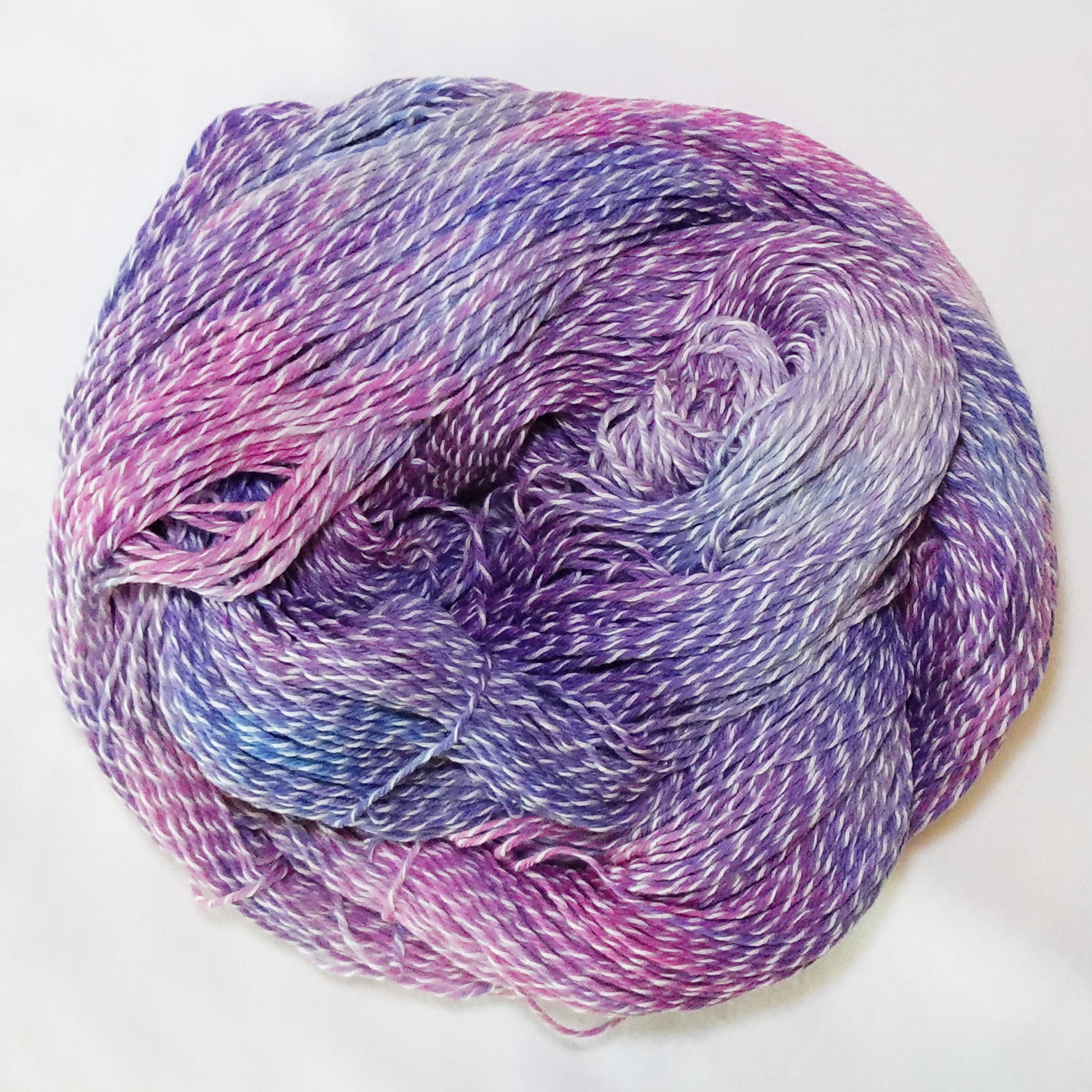 Hand-dyed white zebra base fingering weight yarn in lilac, orchid pink, and periwinkle blue with white plied throughout.