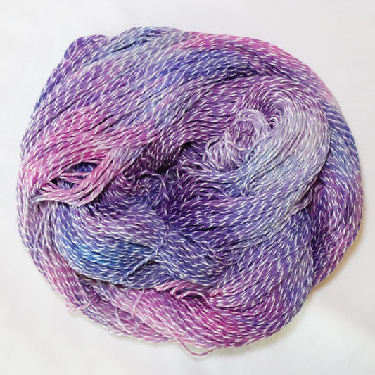 Hand-dyed white zebra base fingering weight yarn in lilac, orchid pink, and periwinkle blue with white plied throughout.