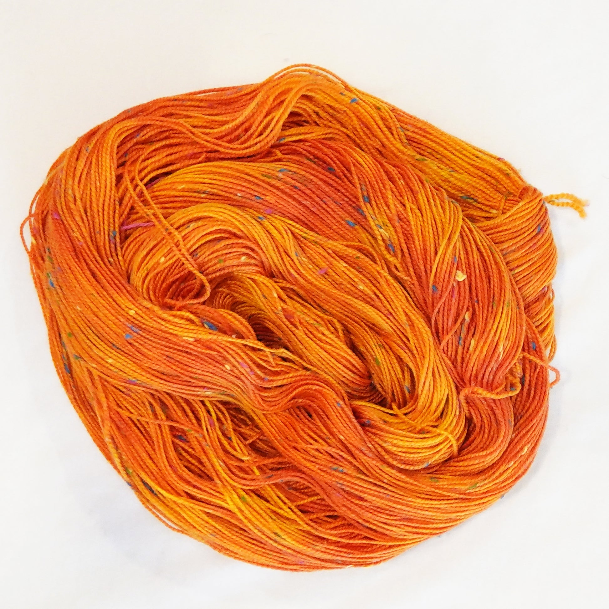 Hand-dyed yarn in vibrant orange tones with colorful flecks — bold, warm, and inspired by blooming tiger lilies.
