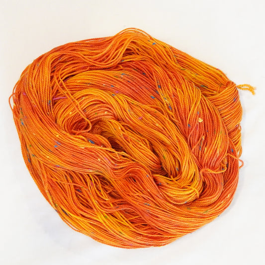 Hand-dyed yarn in vibrant orange tones with colorful flecks — bold, warm, and inspired by blooming tiger lilies.