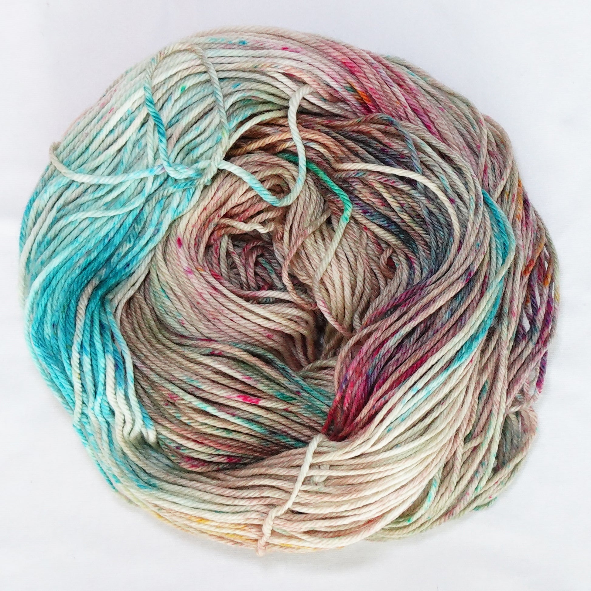 Hand-dyed worsted weight yarn in warm sand with teal, coral, and pink speckles throughout.