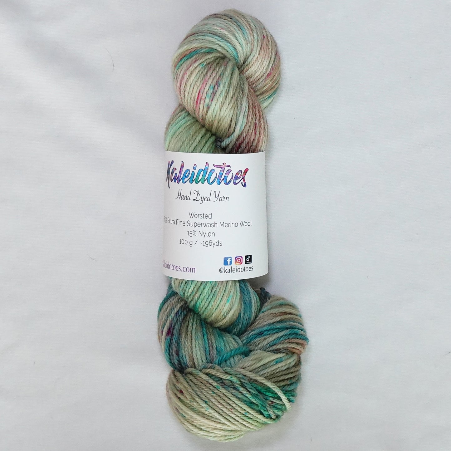 Hand-dyed worsted weight yarn in warm sand with teal, coral, and pink speckles throughout.