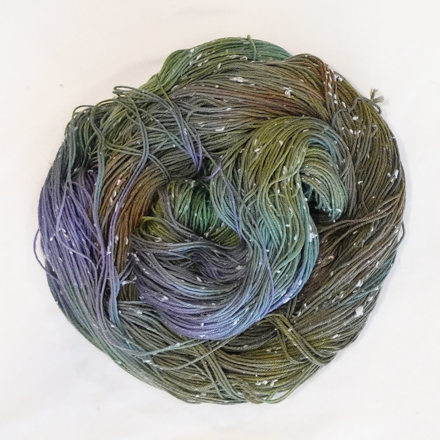 Hand-dyed yarn in moody green, olive, and muted violet tones with soft white flecks — earthy, atmospheric, and softly blended.