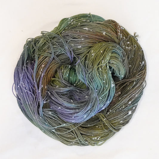 Hand-dyed yarn in moody green, olive, and muted violet tones with soft white flecks — earthy, atmospheric, and softly blended.
