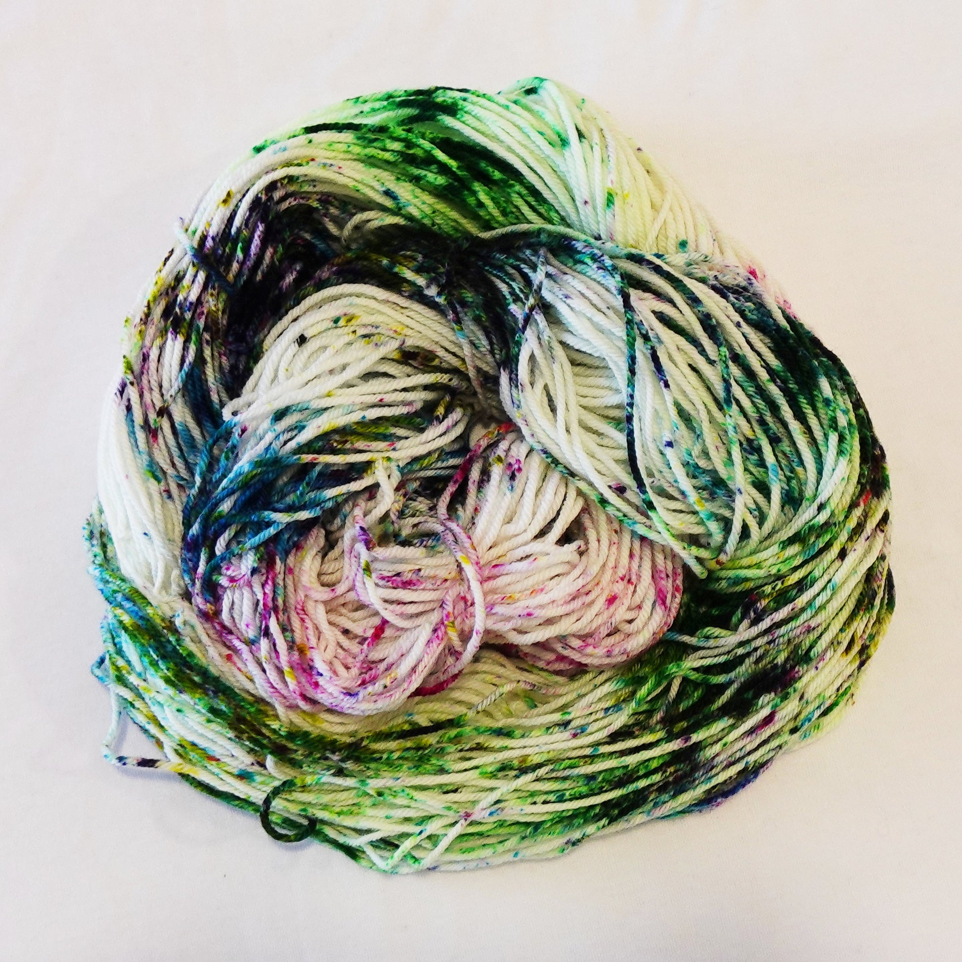 Hand-dyed yarn skein with bright floral speckles in purple, pink, green, and blue on a light base